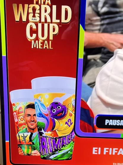 A cropped photo of TV graphic about the “FIFA World Cup Meal” with two illustrated cups. The one in front has a smiling purple Grimace wearing a yellow jersey making a save.
