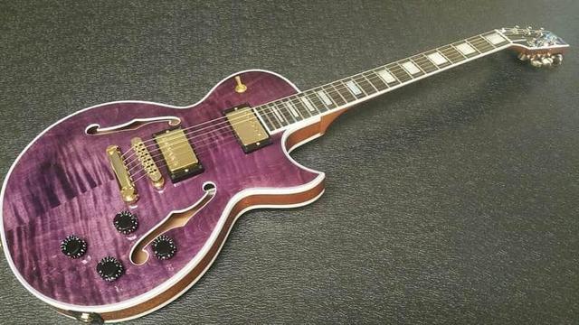 A very classy purple guitar lying on textured black vinyl and photographed from a low angle.