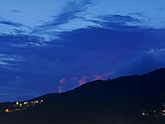 A post-sunset with a silhouetted hill in front, appearing to be leaking magenta into the atmosphere even as dark background clouds loom.