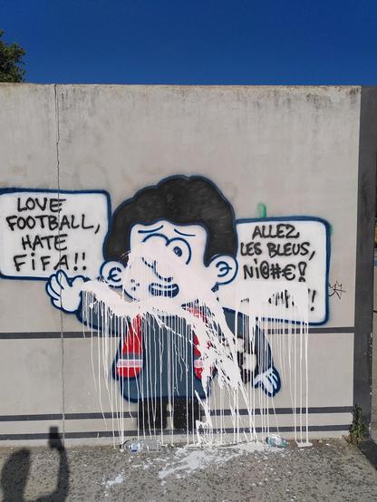 Le personnage de tapas nocturne, mais brun, avec un tshirt bleu et une chasuble rouge, tenant un ballon de foot, qui dit :
- love football, hate fifa !!!
- allez les bleus, ni@#€! les fafs !!

De la peinture blanche a été jetée sur le visage, les bras et le texte "les fafs"