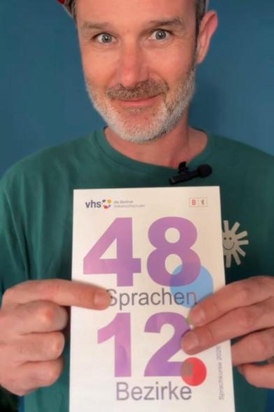 Ein Mann hält den neuen Sprachleitfaden mit der Aufschrift „48 Sprachen 12 Bezirke“ der Berliner Volkshochschulen in die Kamera.