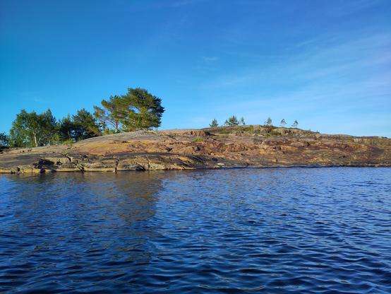 A rocky shore between blue water and blue skies, this time smooth and polished, raising slowly from left to right.