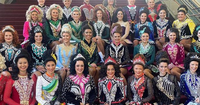 Irish Dancers pose for a group photo, sitting on stairs in their flamboyant, colourful dancing costumes.