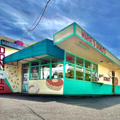 Marie's Donuts, a cute little mid-century style donut shop taken from a very low angle upward. There is a blue sky with wispy clouds beyond.