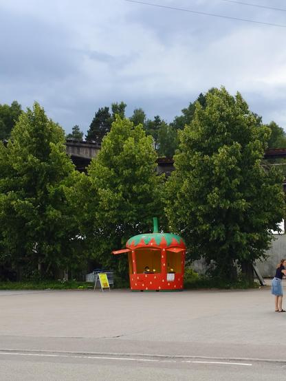 A photo of a wooden stand selling strawberries. The stand is in the shape of a strawberry.