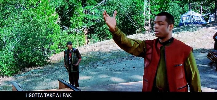 Star Trek First Contact scene. We're in a clearing outdoors with thicc green forest and camping tents in the background. We see Zefram Cochrane (a human guy) further back looking up towards Geordi, and Geordi up close, on some kind of platform or stage. He's posing, holding one arm up and out, as if getting handed something from someone above. Both he and Zephram are wearing civilian clothing, outdoorsey "I own a kayak" type stuff. 
Closed caption reads, "I gotta take a leak."
