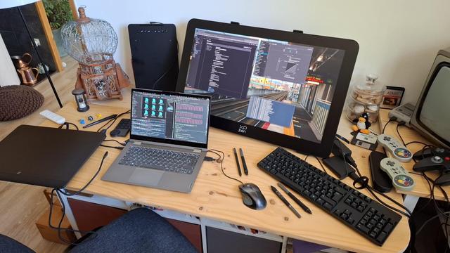 My "dev workbench setup" with laptop displaying code and directories (kate, a konsole for compiling and dolphin to see the file changed), surrounded by multiple drawing tablets (the Artist Pro 16 gen2, the Deco 01V3 , to test the bpf support too during dev). In the middle, a large 27-inch XpPen Artist Pro (gen2) tablet dominates the desk. Around some decoration for the shooting of the video review: RPG dices, an old TV, and controller of super nes and n64. A little plushie of tux also seat in a corner.