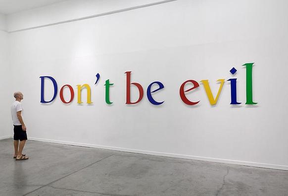 A person in summer clothing stands in front of the inscription "Don't be evil!" which was formerly Google's motto, and a phrase used in Google's corporate code of conduct around the year 2000.