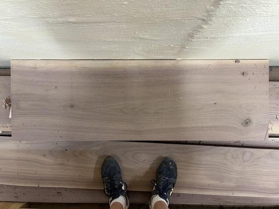 A straight down shot of a wide walnut board. The photographers two feet showing in front of the board.