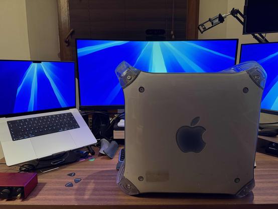 A desk with MacBook Pro and monitors and old Power Mac G4