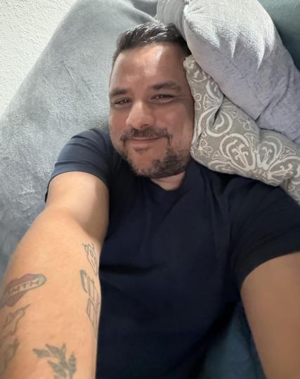 Me, lounging comfortably on a couch, smiling at the camera. I have short hair and are wearing a dark shirt. I'm cozy.
