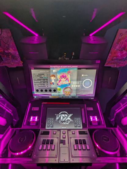 wide image of the main section of a iidx lightning model arcade cabinet. it has a large main monitor and a touch screen, and its controller section shows a turntable + 7keys layout on each side. its LEDs illuminate the entire thing pink. it looks futuristic and very cool. kira has the default qpro avatar set which looks like a plain dude with brown hair