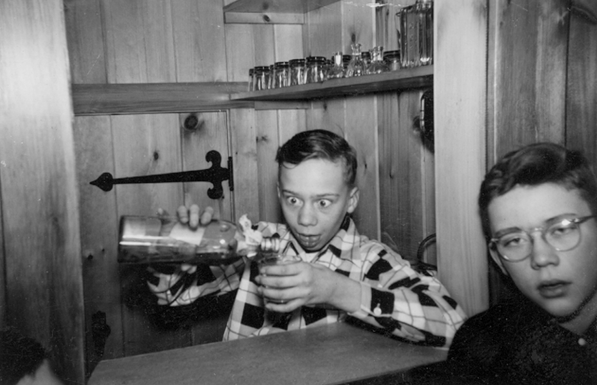 a picture from my mom's photo album showing two young men at a bar in someone's house pouring some booze.  The bartender looks like a psychotic Don Knotts; the customer like a hammered Paul Dano.
