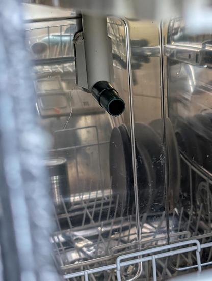 Innenansicht einer Spülmaschine mit einem improvisierten Ersatzteil am Wasserzulauf: Anstelle der abgebrochenen Einspritzdüse sitzt eine grüne Tülle, die perfekt in den Trichter der Spüharme passt