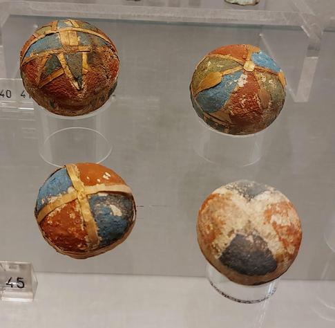 A close-up of four decorative balls featuring chipped and faded geometric designs in blue, orange, and beige, displayed in a museum exhibit.