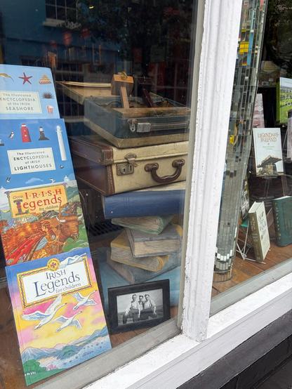 A bookshop window display with an old suitcase, a box of woodworking tools and a black and white photograph of three young men from the 1940s