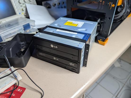 Pair of optical drives stacked on top of each other with an open PC in the background