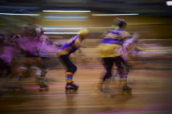 A long exposure image of roller derby competitors from the Beauty School Knockouts (pink), and Team Unicorn (Purple & Gold). 2013/11/09