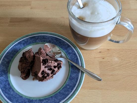 Ein Teller mit Schokoladeneis und eine Tasse Cappuccino auf einer Arbeitsplatte aus Holz