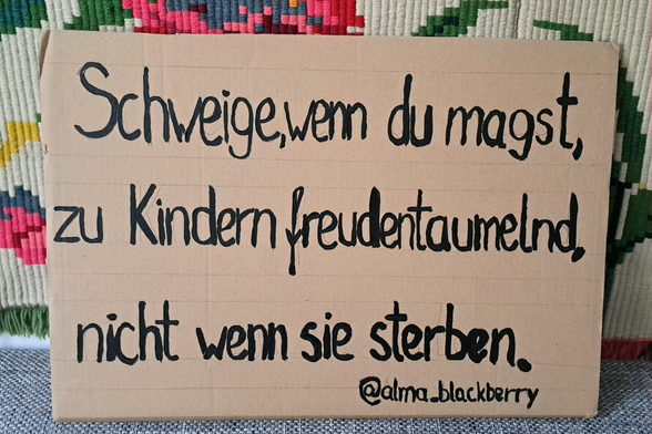 Brauner Karton, schwarze Schrift, alles vor einem textilen Hintergrund:
Schweige, wenn du magst,
zu Kindern freudentaumelnd,
nicht wenn sie sterben.
@alma_blackberry