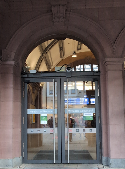 Pixeliges Foto einer Eingangstür mit Glastüren und Bogenfenster.  Über der Tür eine kleine Kamera