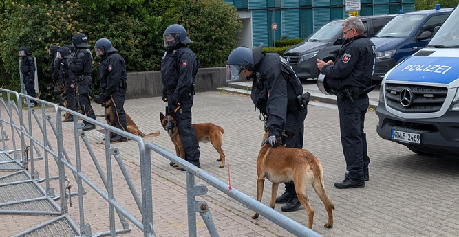 Polizisten mit 5 Diensthunden hinter Hamburger Gittern, dahinter Polizeibusse