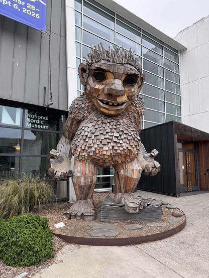 Large wooden troll statue, Freddie Feetsplinters has his hands open by his sides. You can see the entrance to the Nordic Museum behind him.