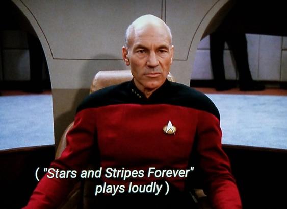 Star Trek The Next Generation scene. We're "on the D" and see Picard in red uniform sitting on the bridge in his captain's chair. Looks like he's stewing about something. (Pun intended) Closed caption reads, "("Stars and Stripes Forever" plays loudly)"
