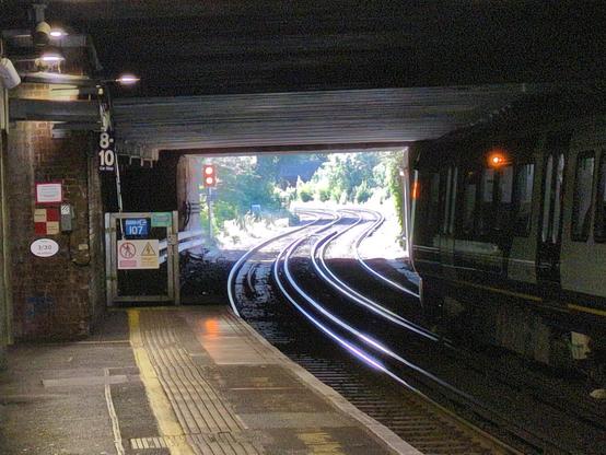 looking along the train line from under the bridge at Richmond station, towards the Twickenham side

as the tracks exit the dark concrete tunnel and emerge into summery greenery, they appear to sway side to side in a pronounced S shaped curve

because of foreshortening this is probably not as severe irl as it appears here, where it looks like the train is going to really swerve side to side