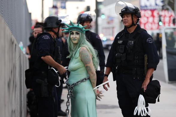 Woman dressed up as the statue of liberty looking at the camera while being arrested surrounding by cops in LA during No Kings protests