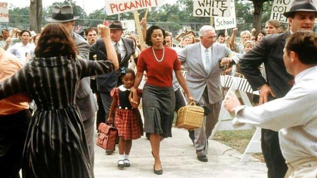 Young Ruby Bridges accompanied by her mother going to school, surrounded by federal agents keeping a crowd with racist signs at bay so she can go to school during the desegregation era.