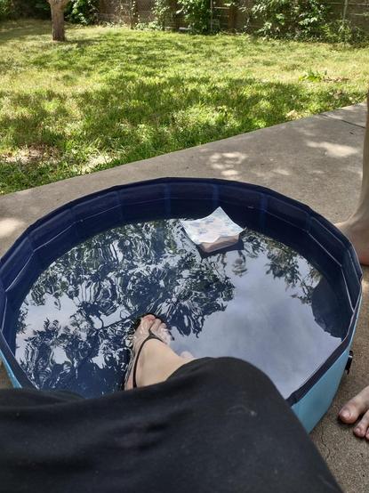 A small collapsible pool with an icepack floating in it and some feet being cool.