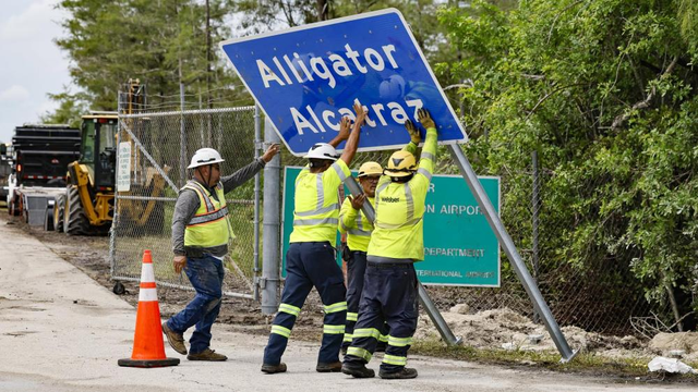 Workers lifting the "Alligator Alcatraz" sign outside the immigrant concentration camp.