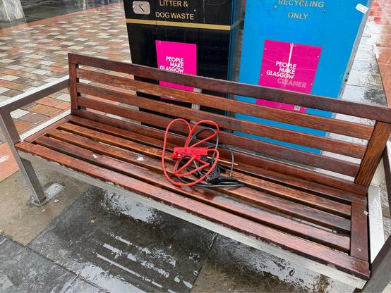 a pair of jumper cables has been abandoned on a wooden bench on a rainy day. there are no cars or even any road nearby.