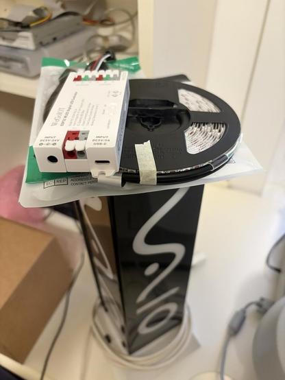 Photo of the Vaio lamp on a desk with an assortment of bits sat on top; a plastic bag for LED tape, the LED tape, and a controller for it.