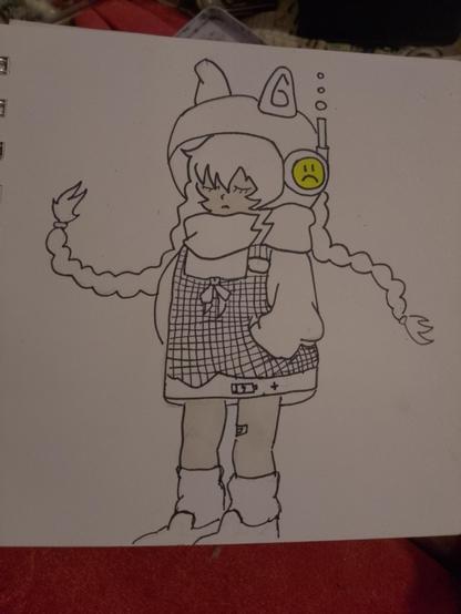 Un dibujo a línea, con algunos toques de color pastel, de un personaje estilo anime de pie y con una expresión melancólica. El personaje lleva un gorro/casco blanco con orejas puntiagudas y un dispositivo lateral con un círculo amarillo que muestra una cara triste. Su cabello, con flequillo desordenado, asoma por debajo del gorro, y dos largas trenzas caen sobre sus hombros. Viste un pañuelo grueso, un suéter holgado y un peto/vestido de cuadros blanco y negro con un lazo en el pecho. En la parte inferior del peto hay un símbolo de batería baja. Las piernas y los pies están cubiertos por botas o calentadores holgados. La paleta de colores es principalmente blanco y negro con tonos muy claros en la piel y el símbolo de la cara triste.