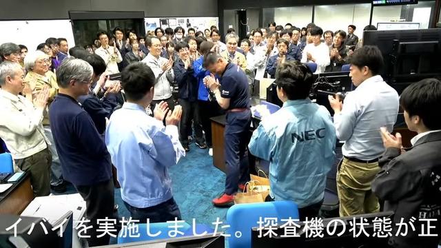 Screenshot from the live stream. In the Hayabusa2 control room, the team gather around the ISAS Director General Fujimoto Masaki, who is clearly delighted.