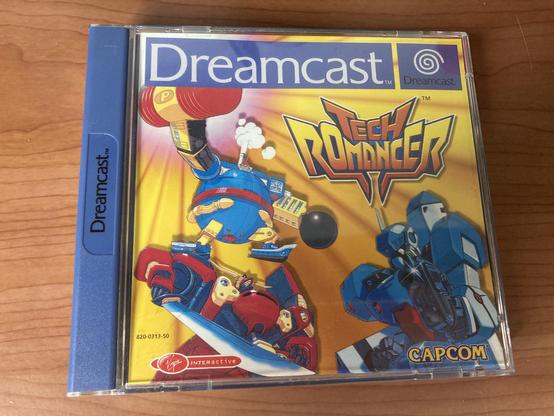A Dreamcast game case featuring the title "Tech Romancer." The cover displays colorful illustrations of robotic characters in a dynamic pose, with the Dreamcast and Capcom logos prominently displayed. The background is vibrant with tones of yellow and orange.