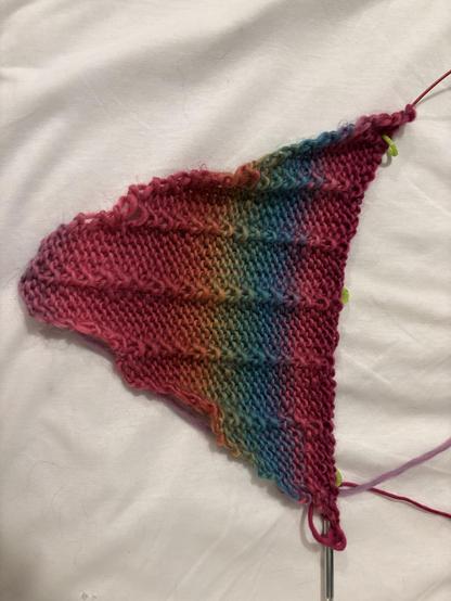 A small triangle of self-striping knit that shifts from magenta to gold to green to teal and back to magenta. Columns of purls form a pattern in the stitch work