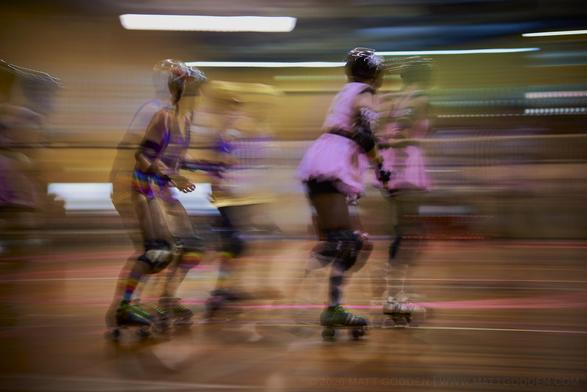 A long exposure image of roller derby competitors from the Beauty School Knockouts (pink), and Team Unicorn (Purple & Gold). 2013/11/09