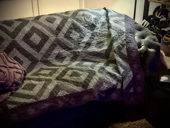 A grey and charcoal quilt in diamond patterns, thrown over a black sofa.