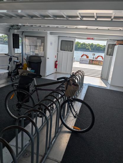 A bike in a center bike rack with a view out the rear of the ferry of floatation rings and river.