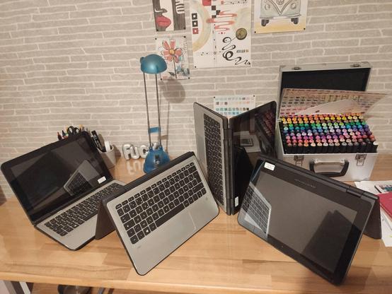 4 ordinateurs convertibles dans des situations diverses, sur un bureau en hêtre, le fond est composé de quelques aquarelles de Madame et dessins variés.
