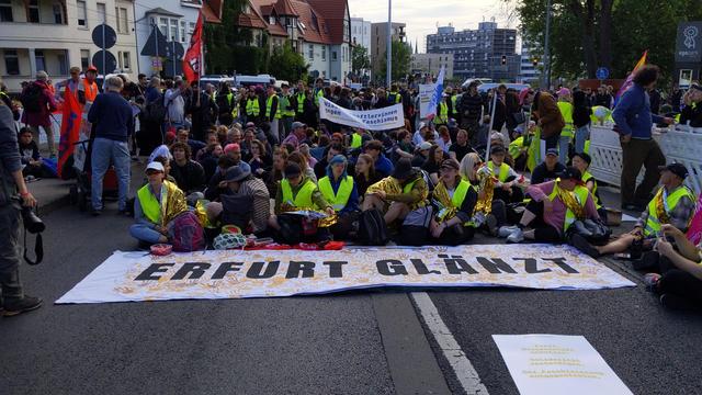 Gruppe von Menschen in gelben Warnwesten hinter einem Banner mit dem Motto der Erfurter Gruppe: Erfurt glänzt