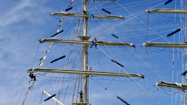 Short version: Sailors on masts. Fuller descriptions: Young sailors dotted around high up on the ropes and cables and riggings and masts of a ship, working on the sails while moored at the Tall Ships Race in Aarhus Denmark (last week). Deep bright blue sky. Coloured bunting on the ships.