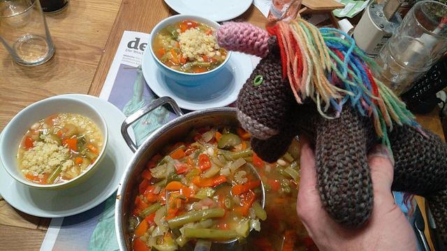 Max, das bunte Strickhorn, mit einem großen Topf Minestrone.