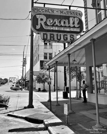 Title: Forgotten Battles

A black and white image of a lone man stands at the corner of the Pilcher & McBryde Rexall Drugs, with the Edmund Pettus Bridge visible off in the distance, on a silent and nearly empty July 4th in Selma Alabama.

July 4, 2021