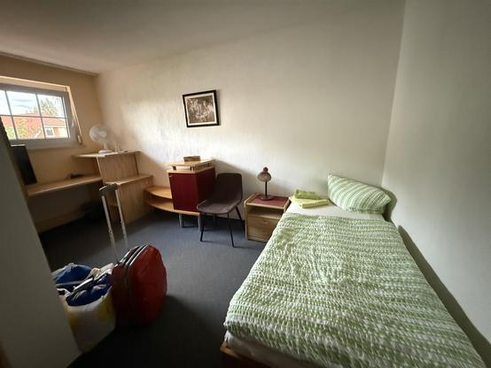 Blick in ein Hotelzimmer, mit lauter Möbeln aus „Kinderzimmerholz“ (billig-Furnier). Rauhputz an den Wänden, und das Fenster ist nur halb (für ein ganzes hat es wohl nicht gereicht). 
Im Vordergrund ein Einzelbett (aus Kinderzimmerholz), mit geün-weißem Bezug. Sieht man nicht, aber es ist aus Plastik. Hmmmm. 
An der leeren Wand hängt ein hässliches Bild in einem hässlichen Bilderrahmen.