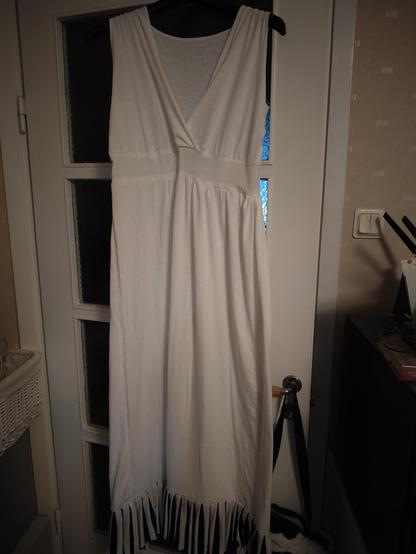 a white jersey dress with a deep V neckline, a high waistband and a black and white flounce at the bottom. it is hanging on a hanger on a door.