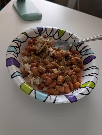 A paper bowl with canned chicken and pinto beans.  Oregano is sprinkled on top.